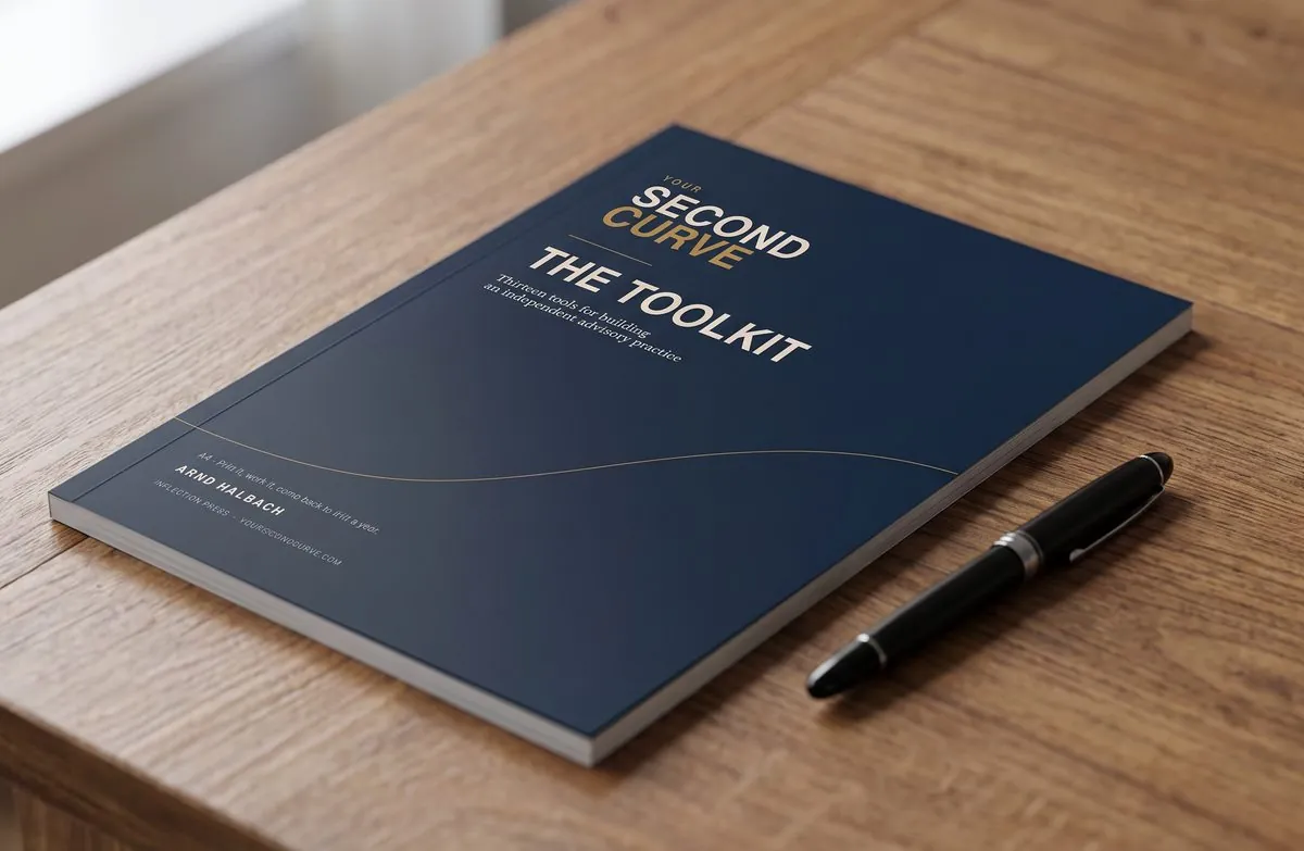 The printed A4 Second Curve Toolkit lying closed on a wooden desk beside a fountain pen, its navy cover reading “The Toolkit — thirteen tools for building an independent advisory practice”.